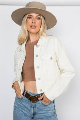 Woman wearing a beige hat, white jacket, brown top, and blue jeans on a white background