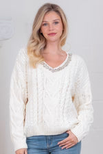 Woman wearing a white cable knit sweater against a plain background