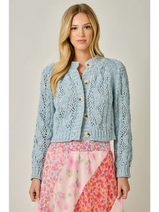 Woman wearing a light blue knitted cardigan over a floral dress on a plain background