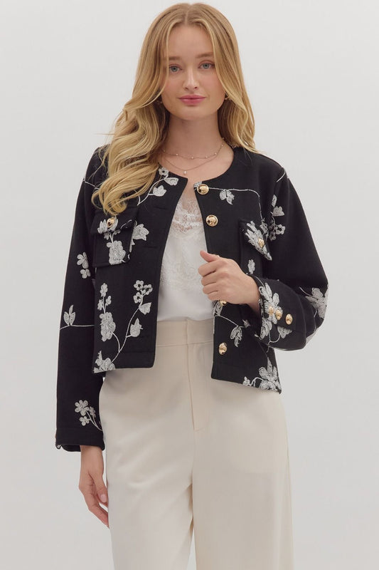 Woman wearing a black floral embroidered jacket on a white background
