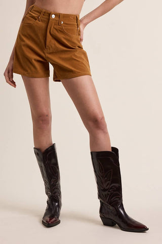 Person wearing brown corduroy shorts and black cowboy boots on a beige background
