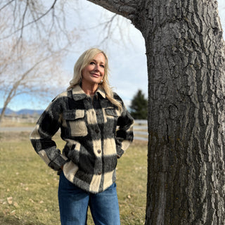 Woman in a plaid shirt standing next to a tree in an outdoor setting