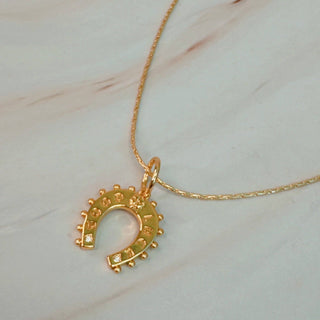 A gold-colored horseshoe necklace on a marble surface.
