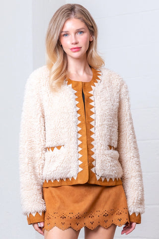 Woman wearing a beige cardigan over a mustard yellow dress with white patterns on a light gray background