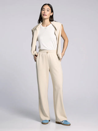 Woman wearing a beige cardigan, white shirt, and beige pants on a light gray background