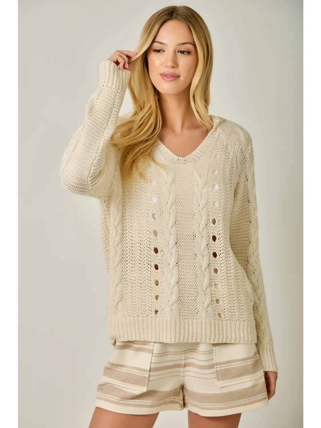 Woman wearing a cream-colored knitted cardigan and shorts on a plain background