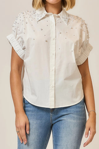 White blouse with lace details and short sleeves worn by a person on a beige background