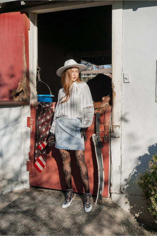 Woman standing in front of a barn with an American flag and a horse.