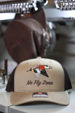 Beige and black cap with duck design and 'No Fly Zone' text on a blurred background