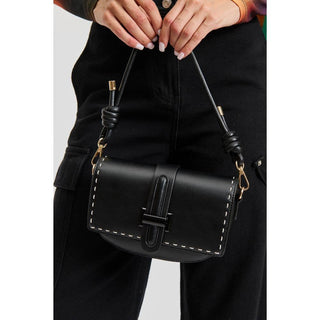 Black leather handbag with gold accents held by a person wearing black pants.