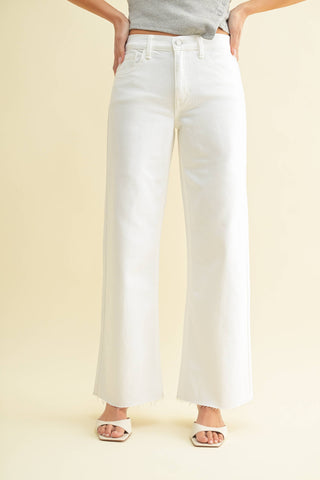 Person wearing white wide-leg jeans on a beige background