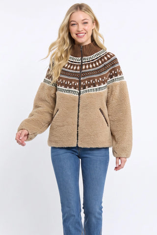 A woman modeling a tan sherpa zip-up jacket with a brown and cream Fair Isle yoke pattern, paired with blue jeans, against a plain white background.