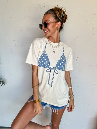 Woman wearing a white t-shirt with a blue polka dot bikini design against a light background