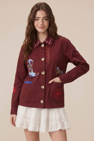Woman wearing a burgundy jacket with embroidered designs on a beige background