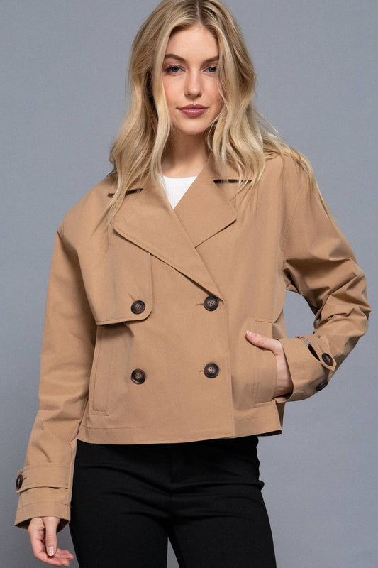 Woman wearing a tan jacket with black buttons on a gray background