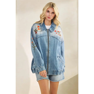 Woman wearing a denim jacket with floral embroidery on a plain background