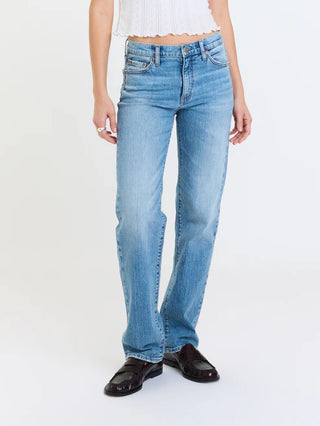 A model wearing light blue straight-leg denim jeans, a white cropped top, and black leather loafers, standing against a plain white studio background.