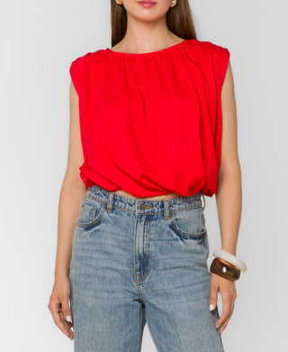 Person wearing a red sleeveless top and blue jeans on a plain background