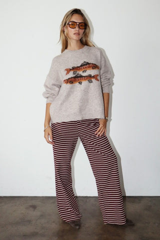 Woman wearing a gray sweater with fish design and striped pants against a white background