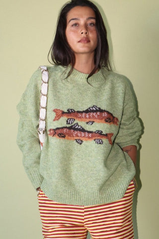 Person wearing a green sweater with fish design and red striped pants against a light background