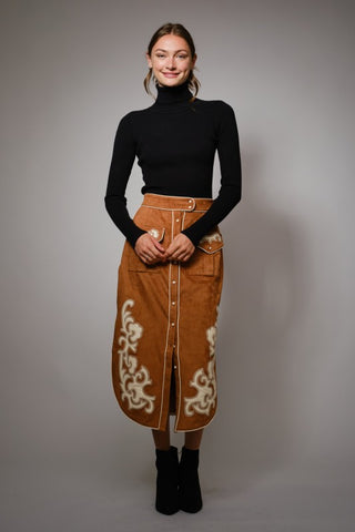 Woman wearing a black turtleneck and brown skirt with white patterns on a gray background