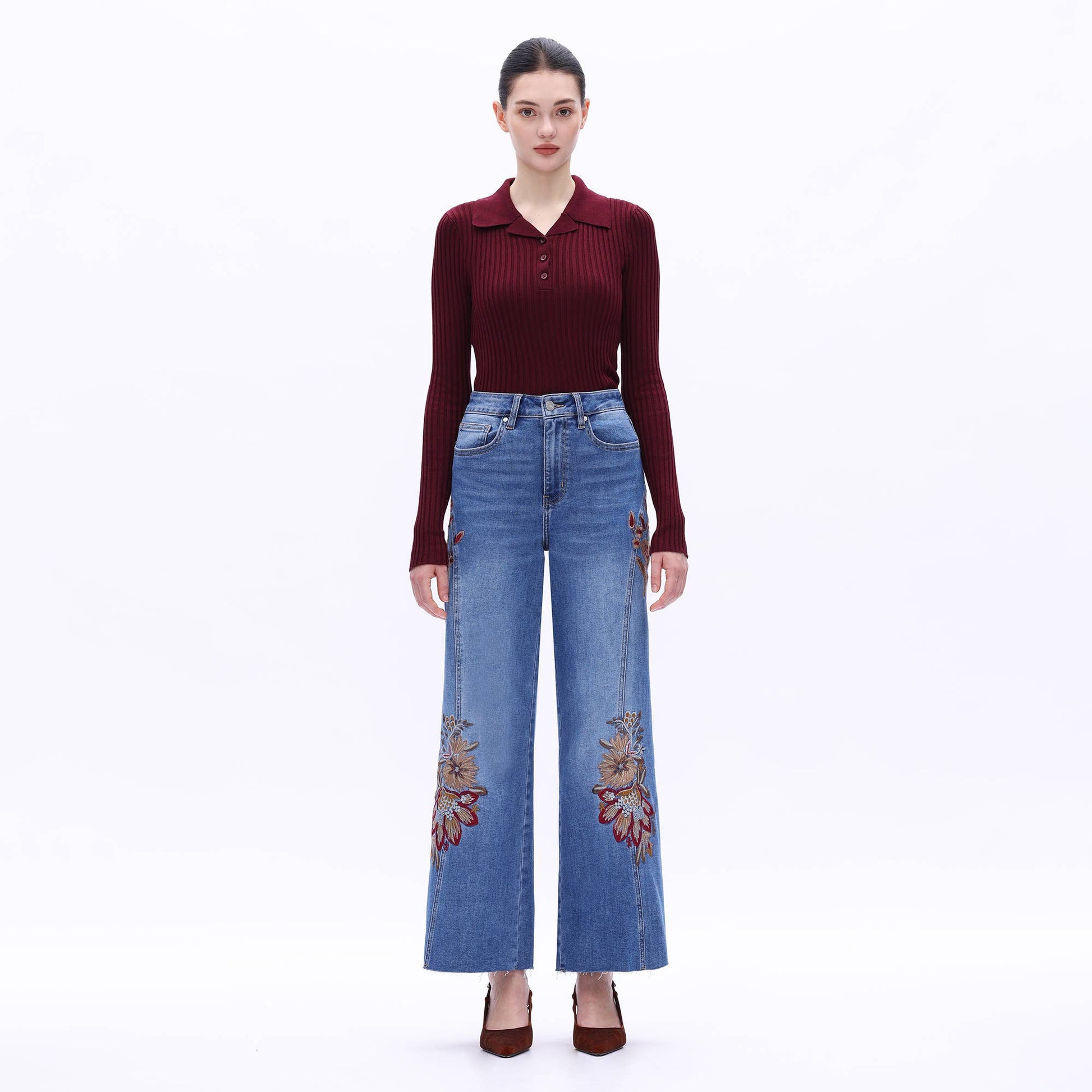 Woman wearing a burgundy top and blue jeans with floral embroidery on a white background