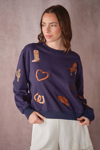 Woman wearing a navy blue sweater with various embroidered designs on a plain background
