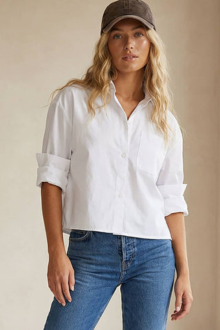 Woman wearing a white shirt and blue jeans with a brown cap against a beige background