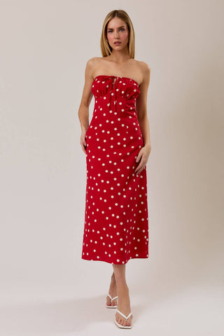 Woman wearing a red strapless dress with white polka dots on a plain background