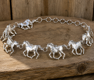 A silver bracelet featuring multiple textured horse charms linked by circular rings, displayed on a rustic wooden surface.