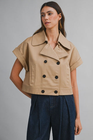 Woman wearing a beige short-sleeve jacket with black buttons on a gray background