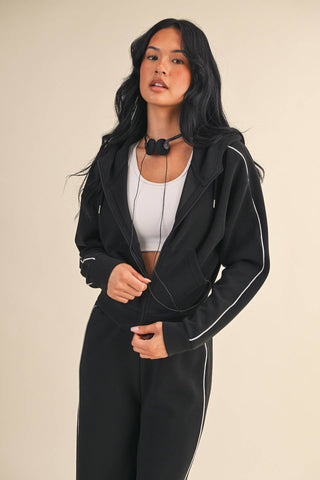 Woman wearing a black tracksuit with white piping on a beige background