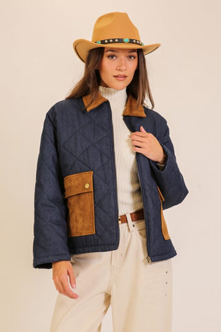 Woman wearing a navy jacket with brown accents and a tan hat on a beige background