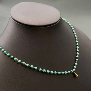 Turquoise beaded necklace with a gold accent on a mannequin bust.