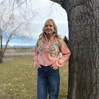 Woman in a pink floral jacket standing next to a tree in an outdoor setting