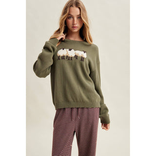 Woman wearing a green sweater with sheep design against a plain background
