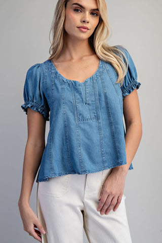 Woman wearing a blue denim top with white pants on a gray background