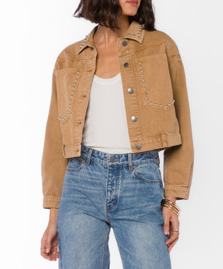 Tan cropped denim trucker jacket with silver studs worn over white tank and blue jeans