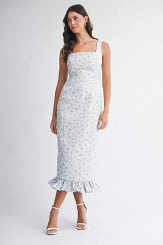 Woman wearing a white floral dress with ruffled hem on a plain background