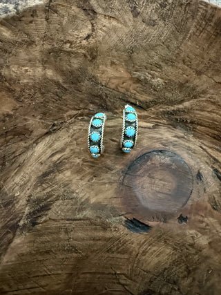 A pair of silver-toned cuff bracelets decorated with round turquoise stones, displayed on a rustic, textured wood slice background.