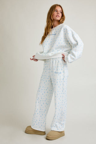 Woman wearing a white sweatshirt and pants with a subtle pattern on a plain background