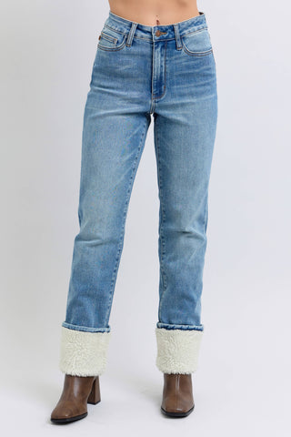Blue jeans with white cuffs worn by a person on a white background
