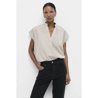 Woman wearing a beige sleeveless top and black pants on a white background