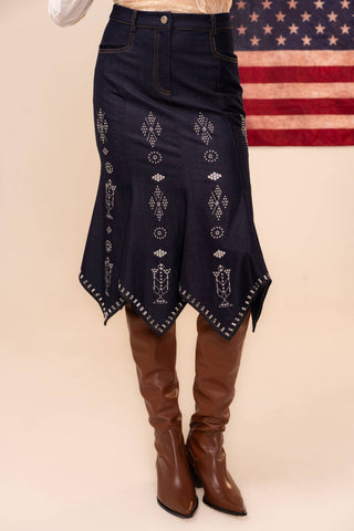 Navy denim skirt with white embroidery and brown knee-high boots on a beige background