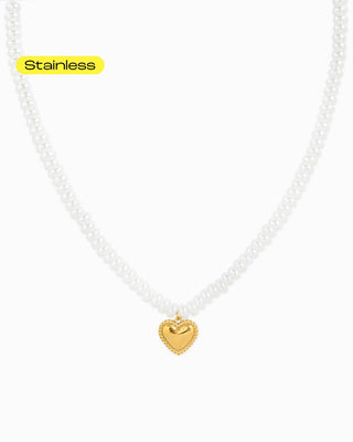 A stainless steel necklace with glossy white pearl beads and a gold heart charm pendant.
