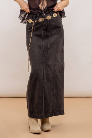 Person wearing a long black denim skirt with a belt on a beige background