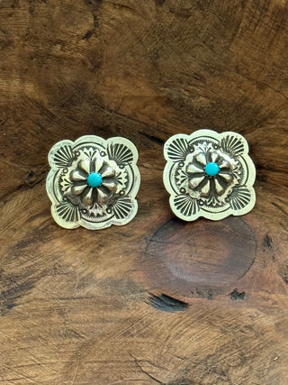 A pair of silver-toned floral stud earrings with turquoise center stones, displayed on a rustic wooden surface.