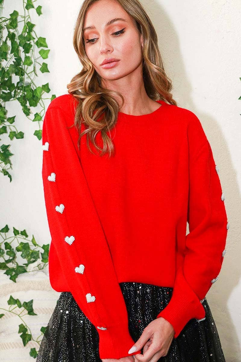 Woman wearing a red sweater with white heart patterns against a light background