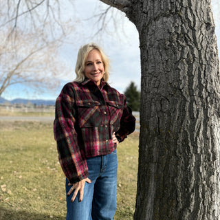 Woman wearing a plaid jacket and jeans standing next to a tree in an outdoor setting