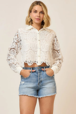 Woman wearing a white lace blouse and denim shorts on a beige background